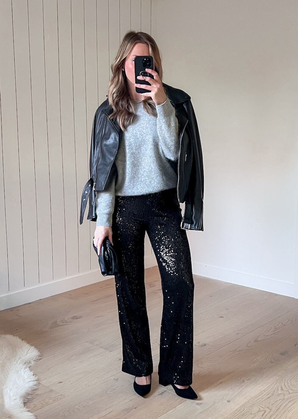 A woman wearing sparkly black wide leg pants with a light grey crewneck sweater, a black leather jacket, and black heels