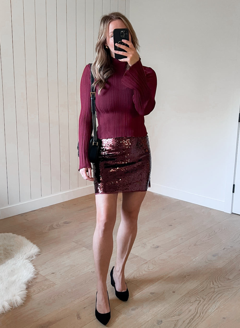 A woman wearing a sparkly burgundy mini skirt with a red knit crewneck sweater and black heels