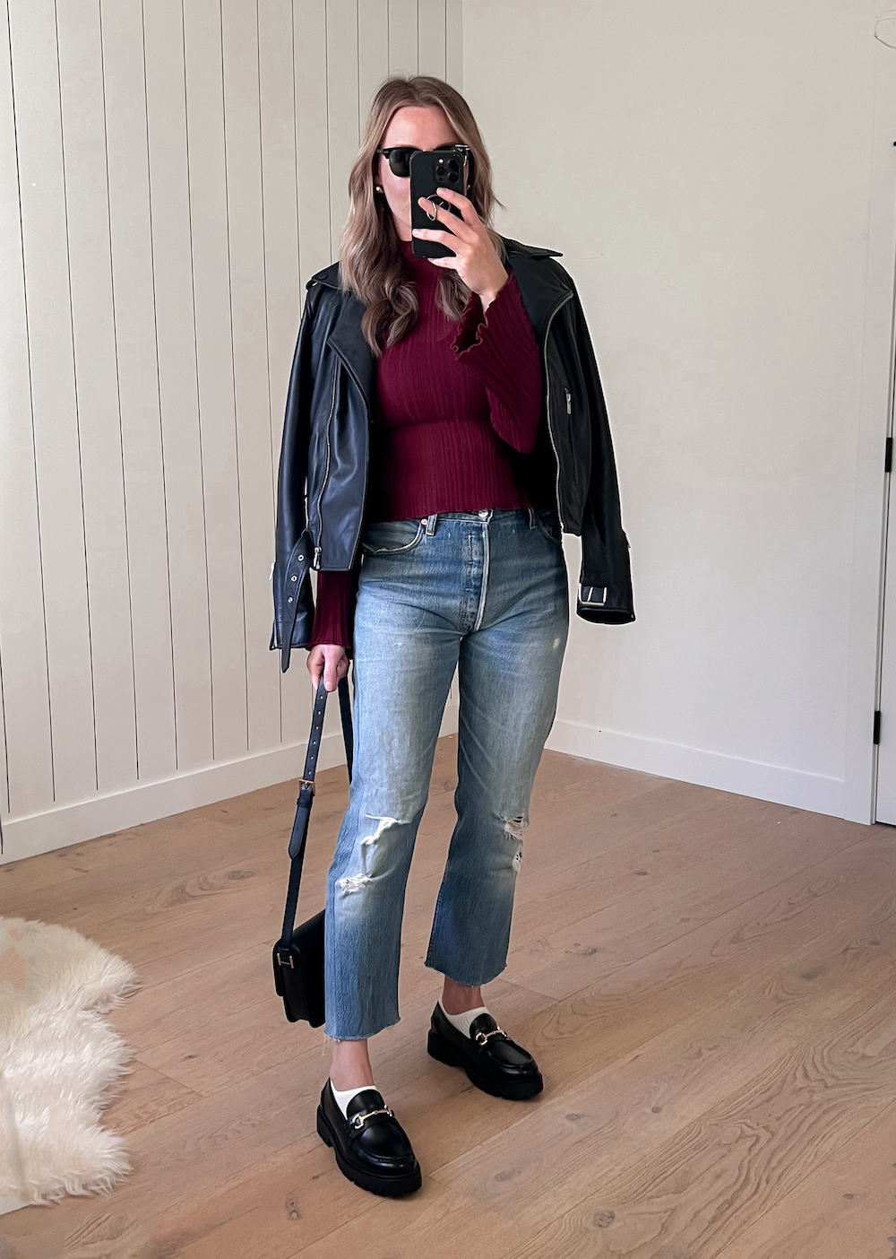 Christal wearing distressed jeans and black loafers with a cranberry sweater under a leather jacket.