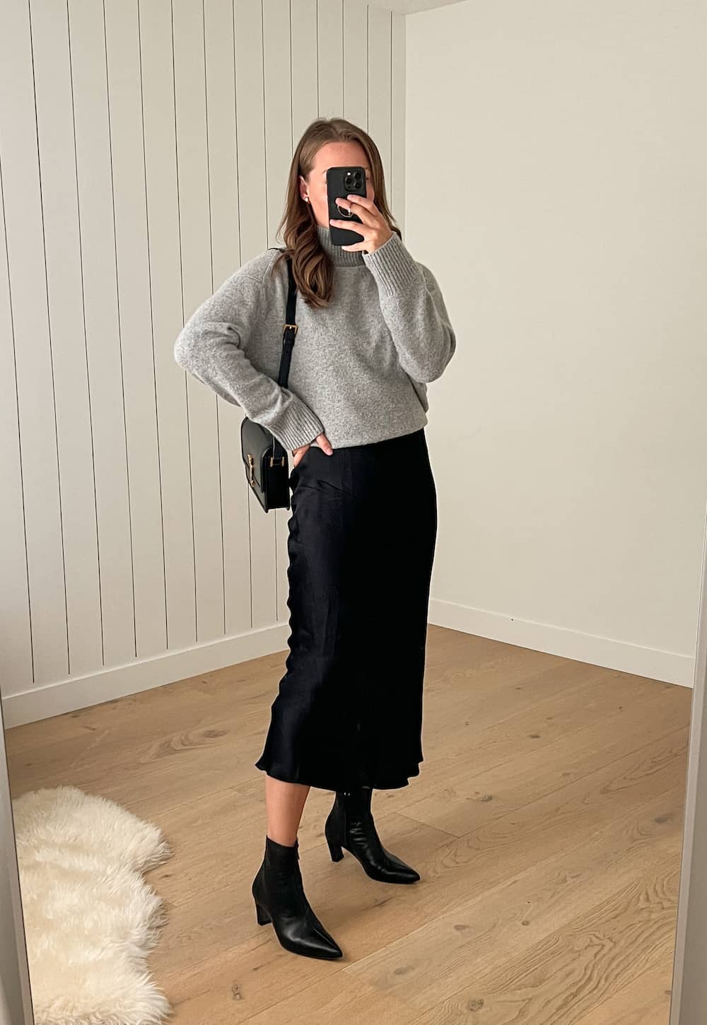 Christal wearing a black slip skirt with a grey sweater and black booties