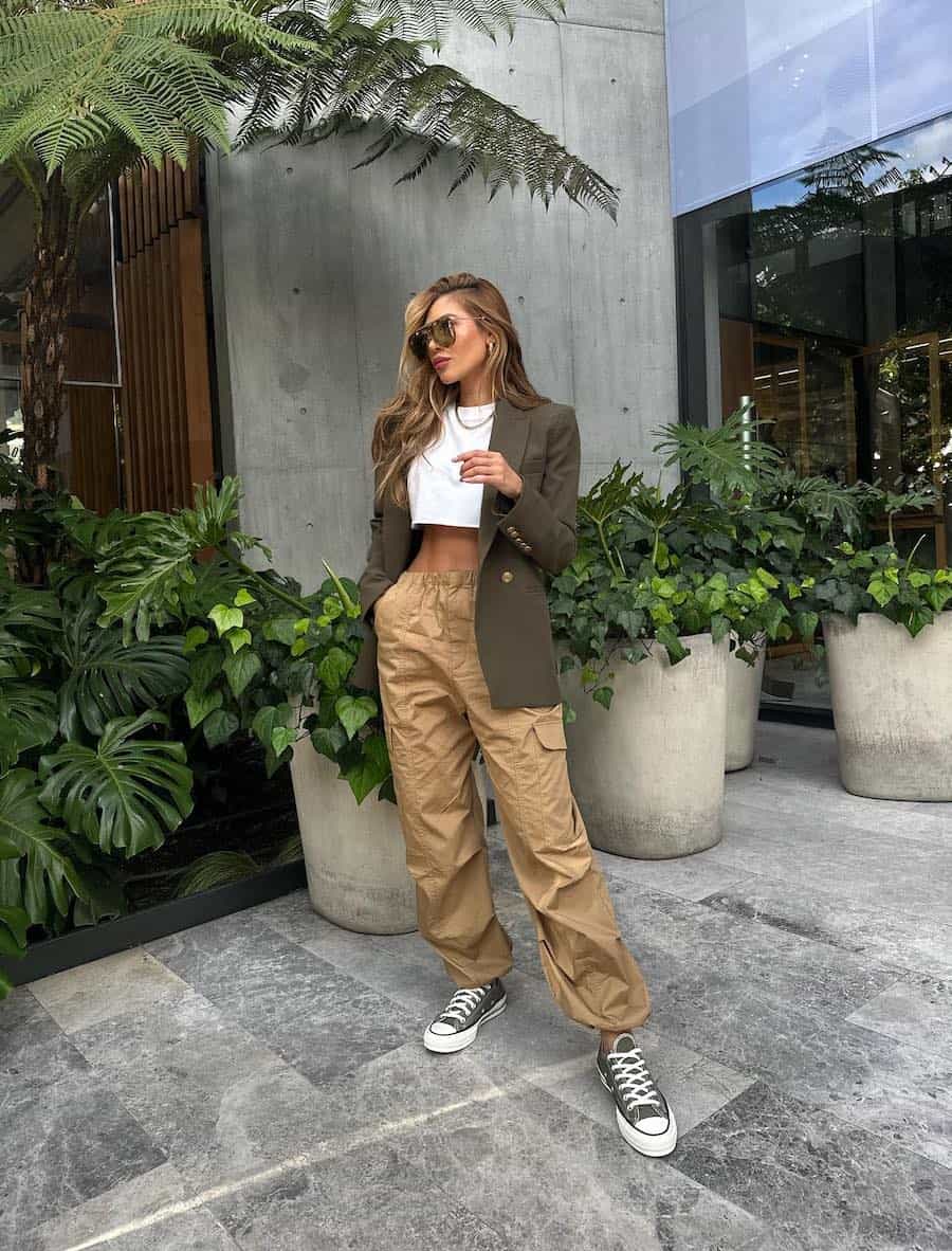 Woman wearing tan cargo pants with a white cropped top and a green blazer with green sneakers.