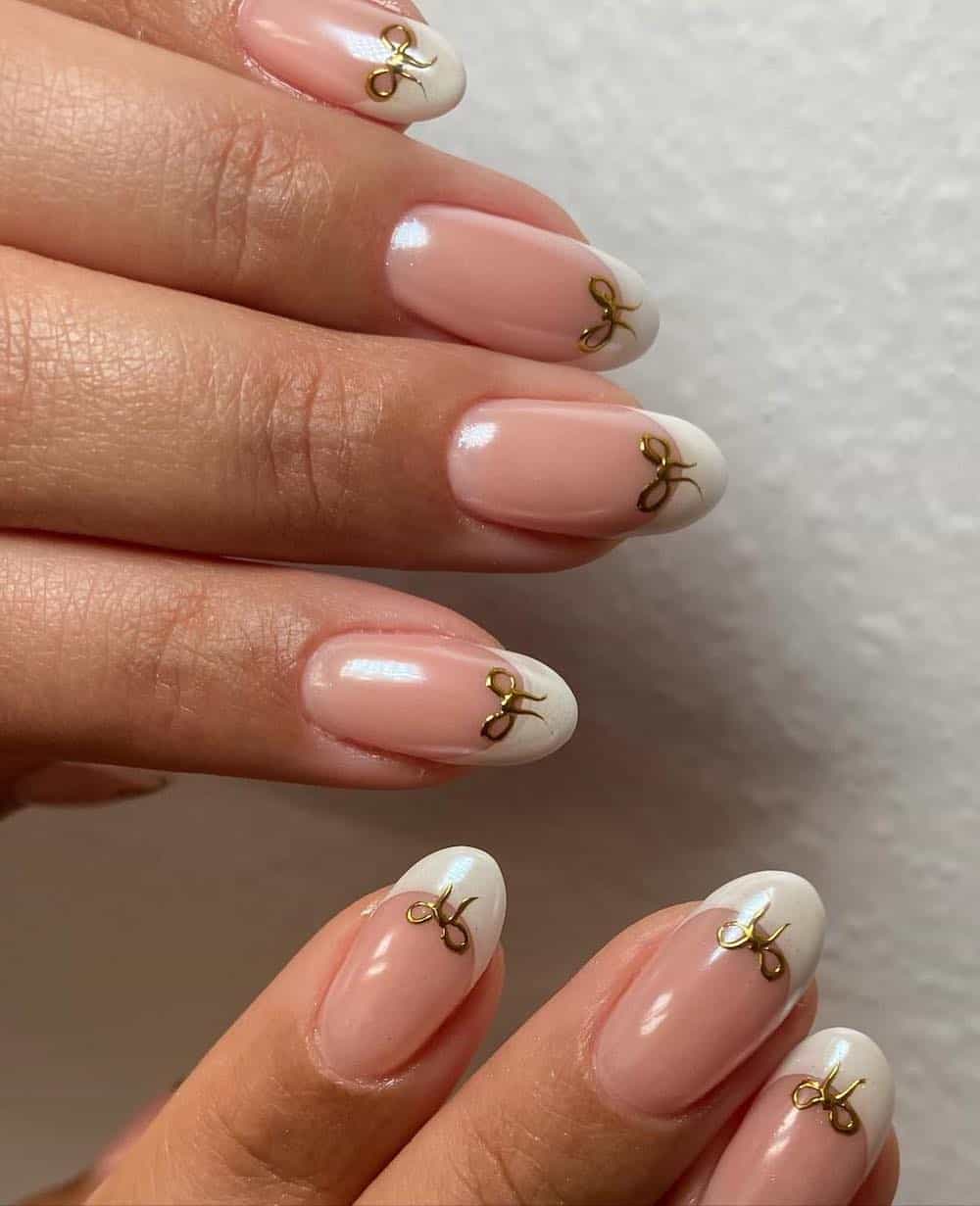 A hand with short almond nails with pearly French tips and golden bows