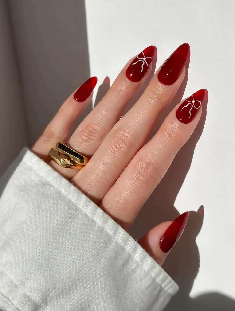 A hand with long red almond nails with white bow nail art accents