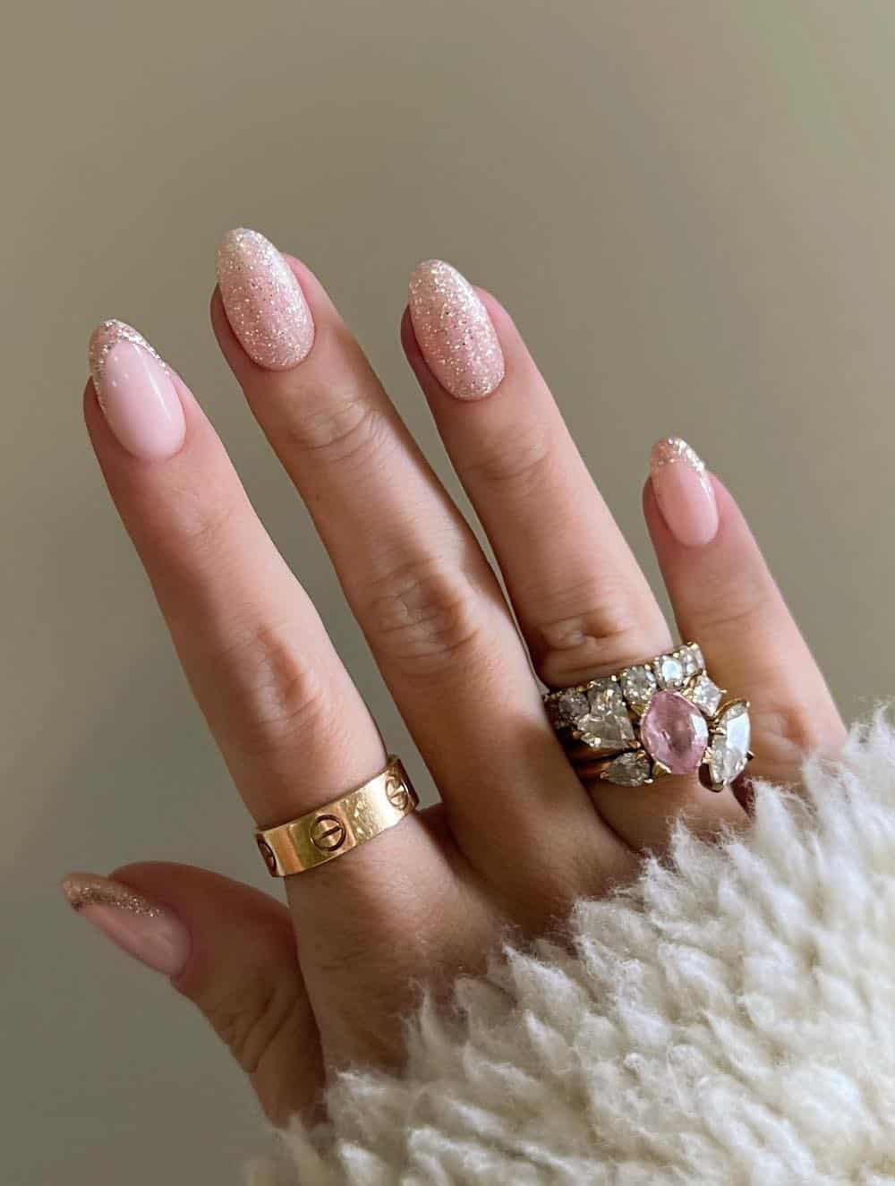A hand with short round nails painted with solid nails and French tips with gold glitter nail polish
