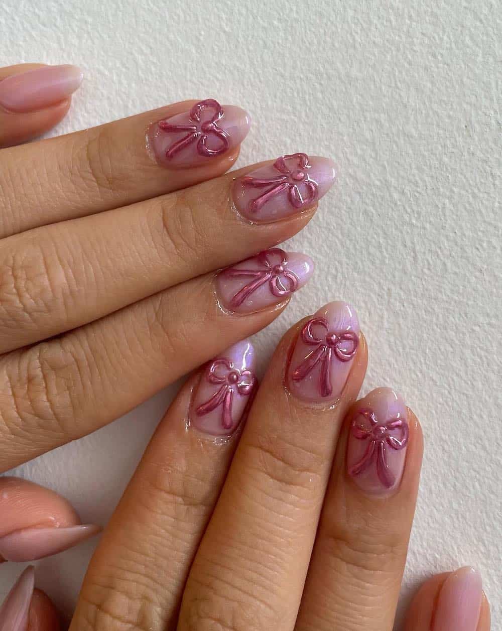 A hand with short shimmering pink almond nails with pink bows