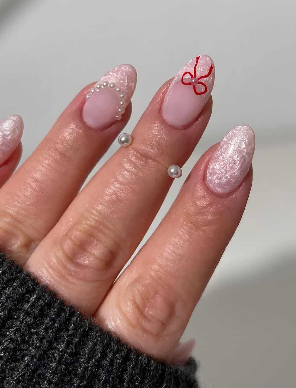 A hand with short almond nails with a pearly pink polish and French tips accented with red bows and pearls