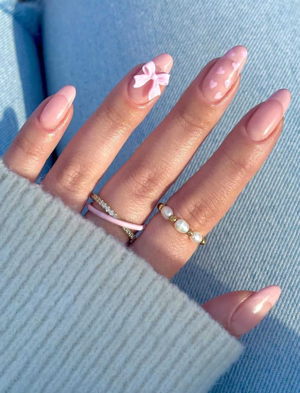 A hand with medium almond nails with pink French tips with heart pattern accent nails and a pink bow charm