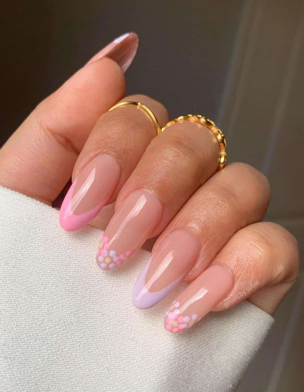 A hand with medium nude almond nails with pink and lavender French tips and floral art tips