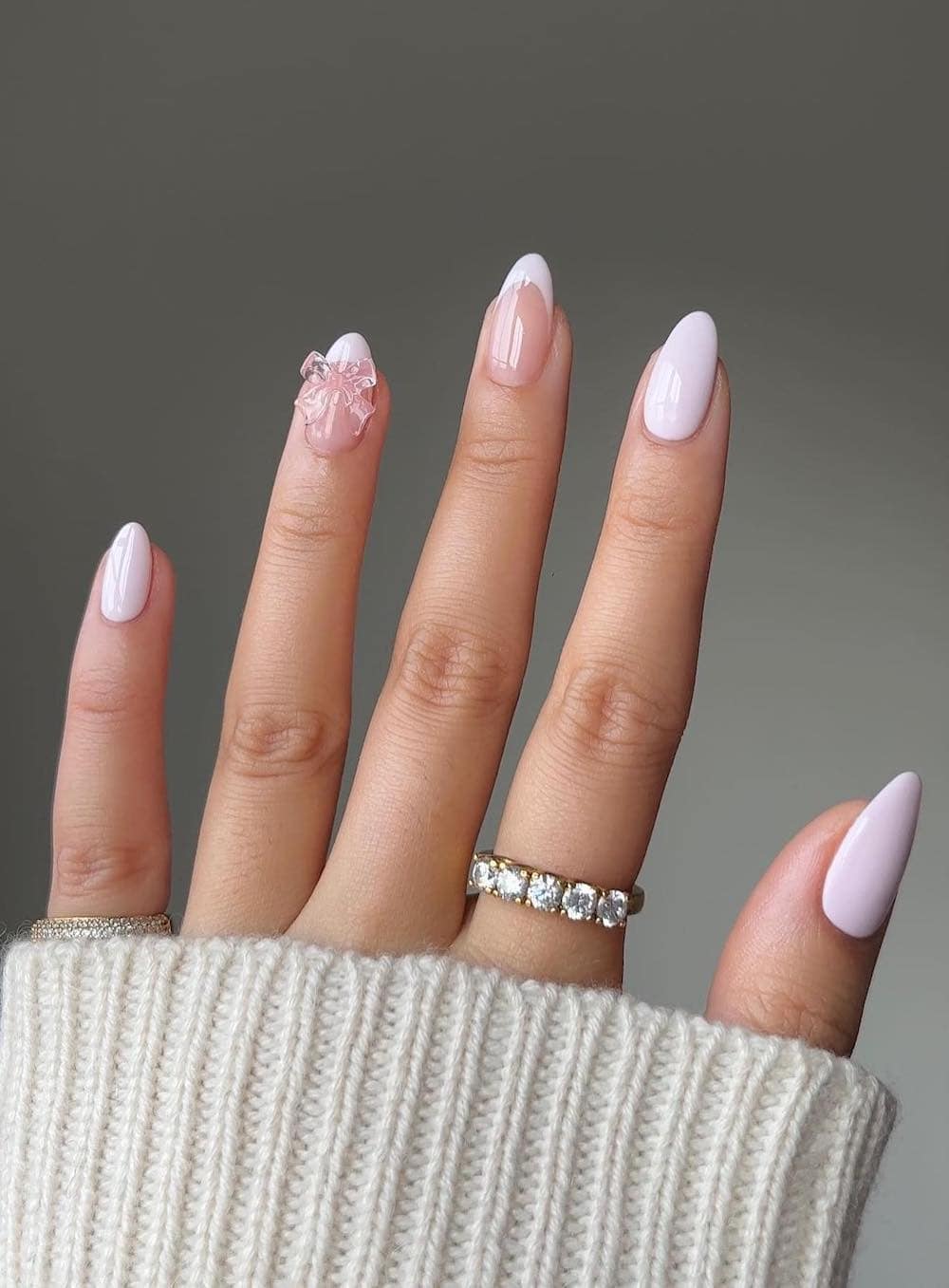 A hand with short almond nails painted a light pink with a sheer pink bow charm