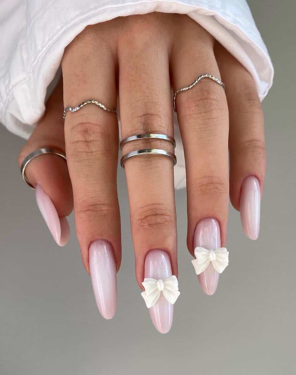 A hand with long almond pastel pink nails with white bow charms