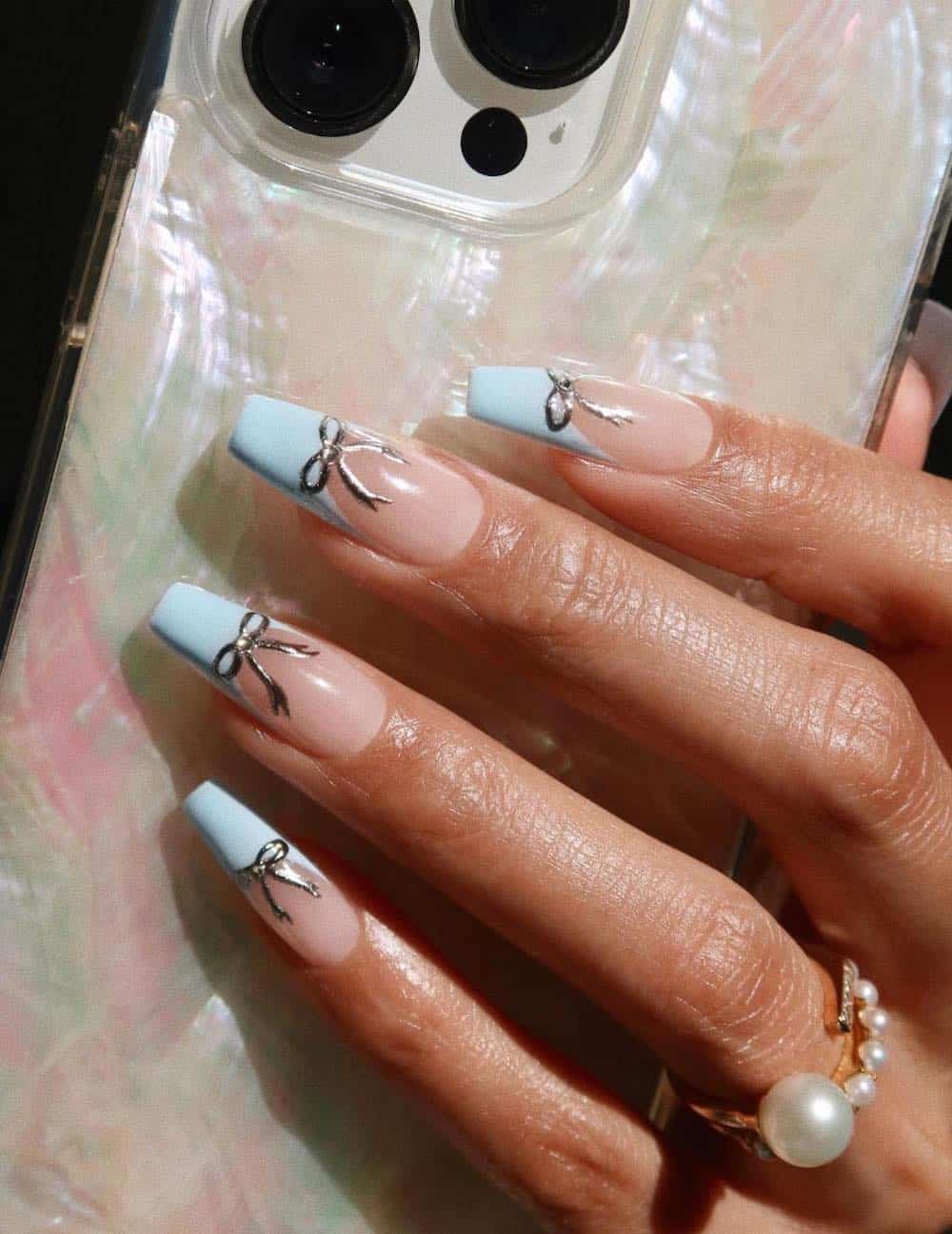 A hand with medium length coffin nails with baby blue French tips and silver bow accents