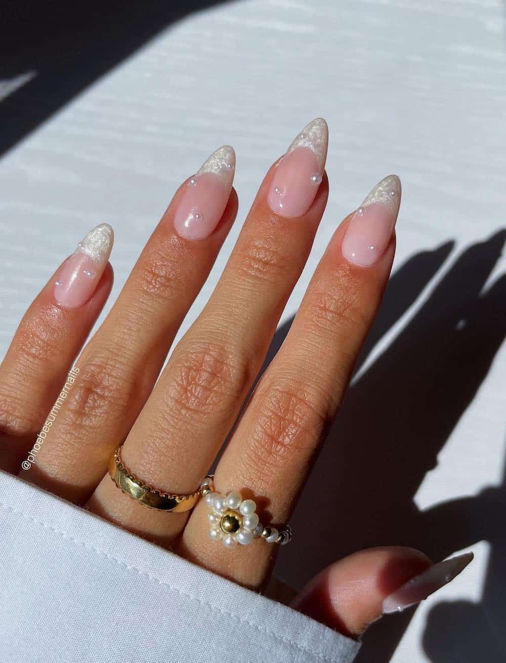 A hand with medium almond nails with white pearly French tips and pearl accents