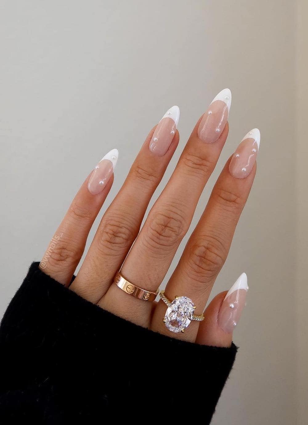A hand with long almond nails painted with white French tips with pearl accents