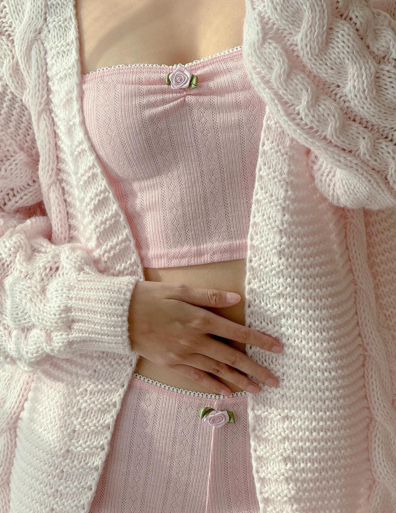 A close-up shot of a woman wearing a matching pink set with rose details and a chunky oversized pale pink cardigan