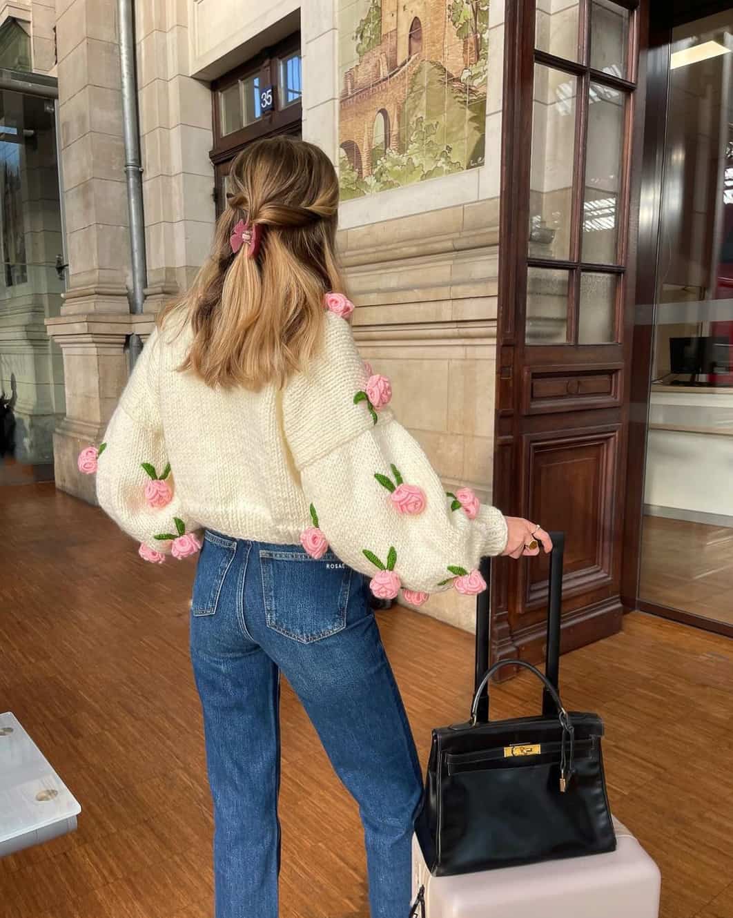 A woman wearing medium blue jeans and a puffed sleeve ivory sweater with pink roses