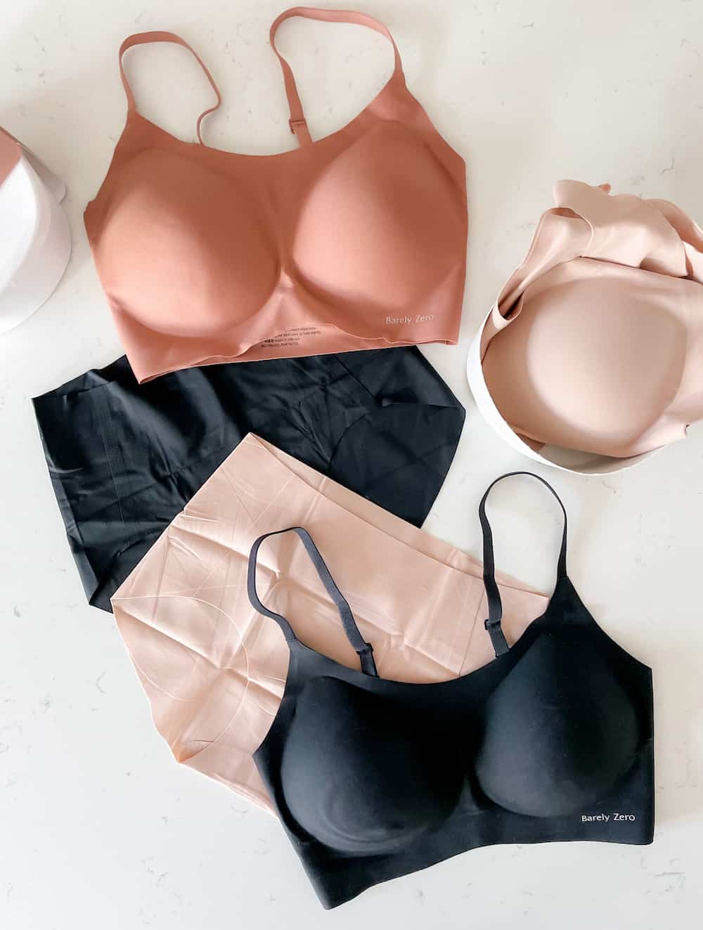 image of three NEIWAI Barely Zero bras on a marble surface in black, and dark nude pink, and two pairs of Barely Zero underwear in black and light pink