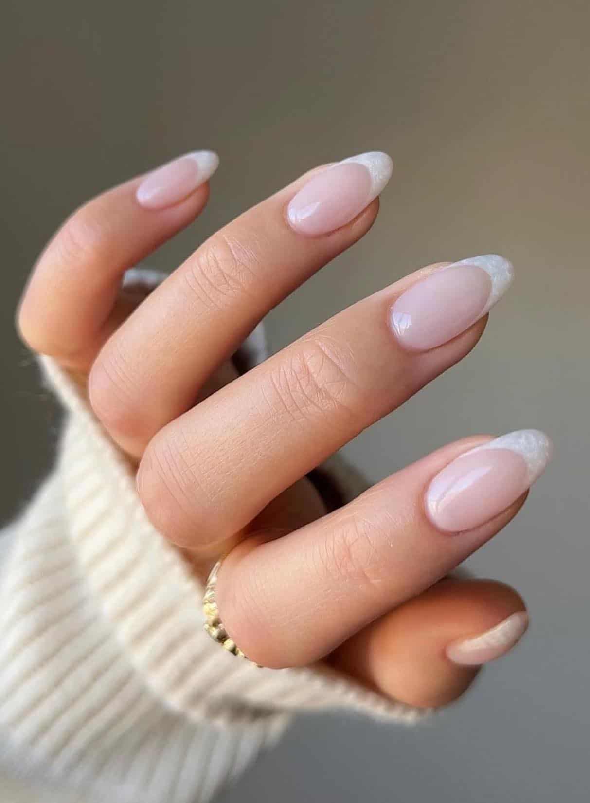 A hand with medium light pink almond nails with pearly white tips