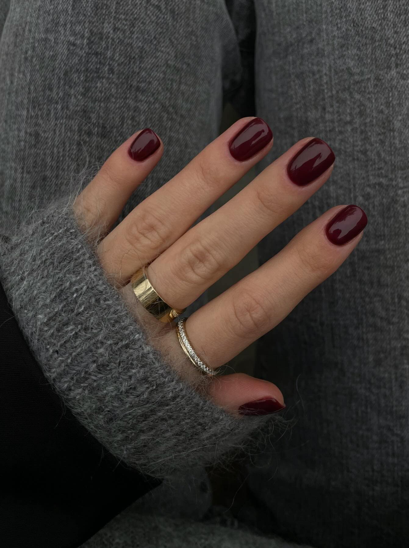 A hand with short squoval nails painted a burgundy red