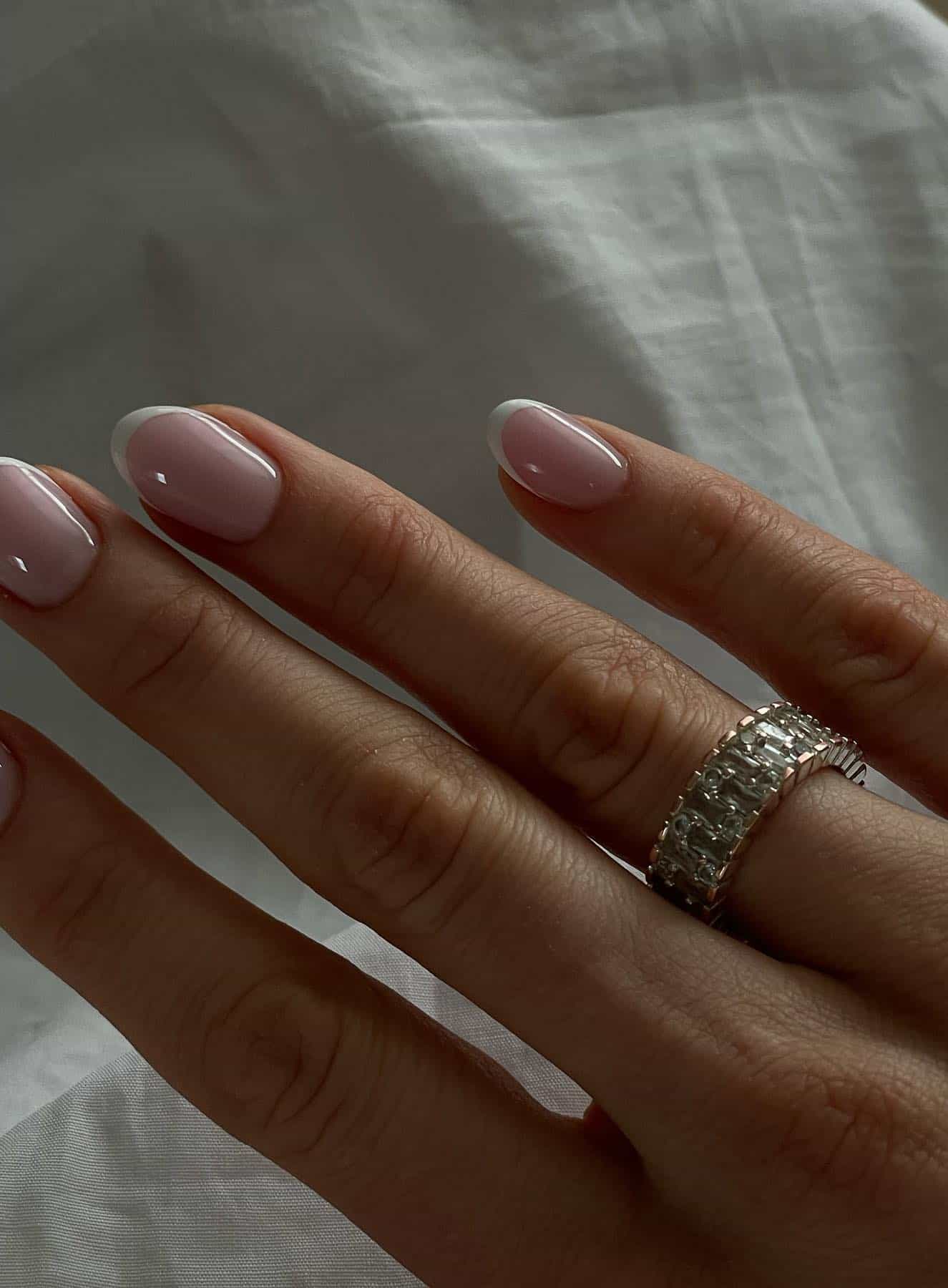 A hand with short round pastel pink nails with white tips