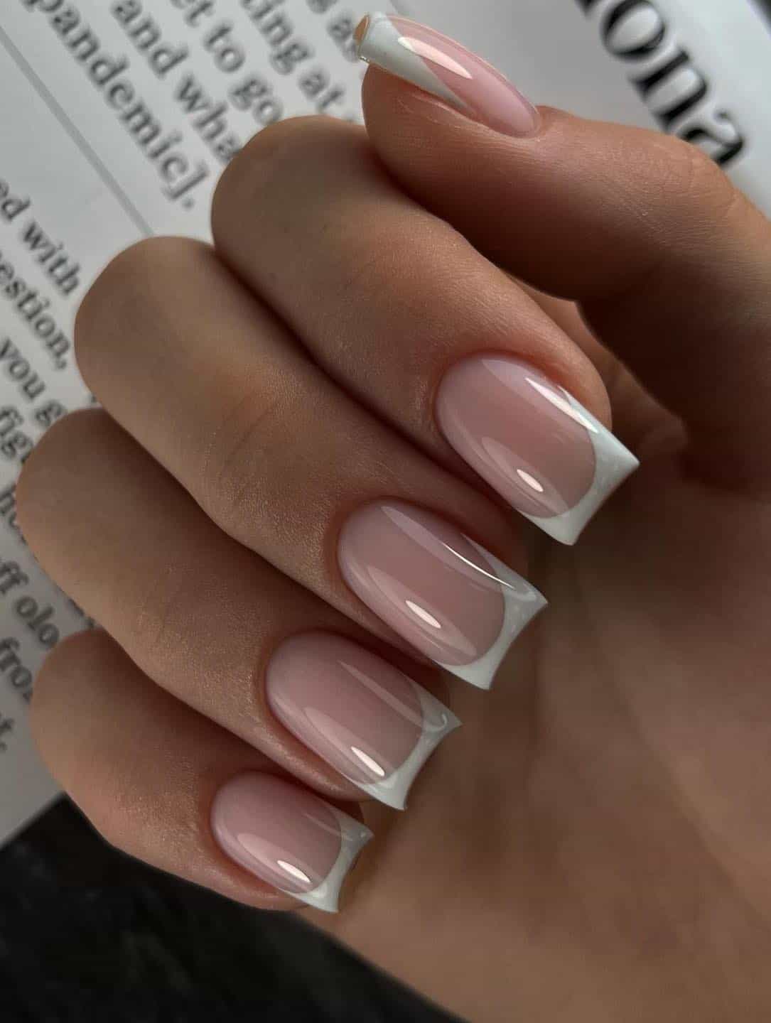 A hand with medium light pink square nails with white tips and a glossy finish