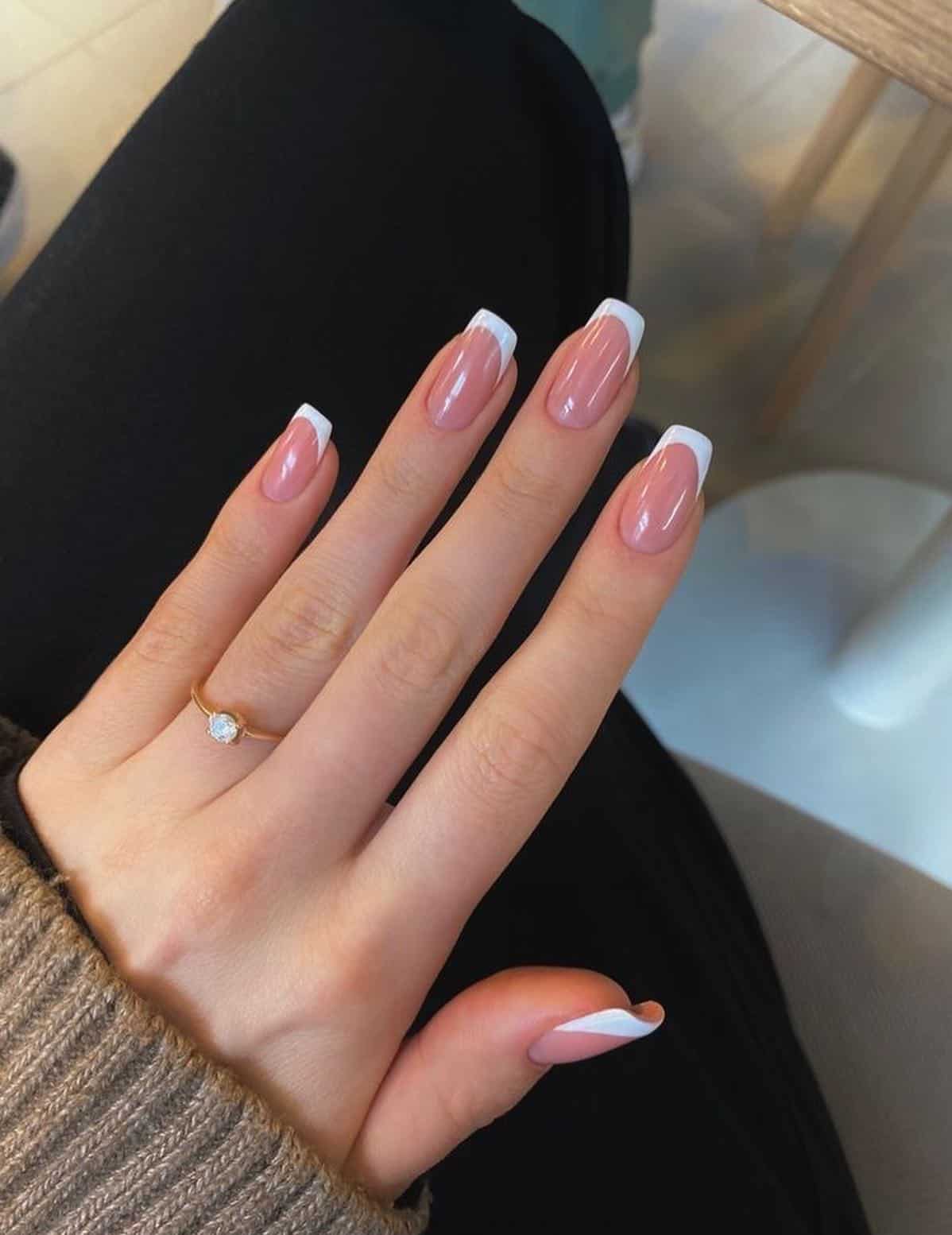 A hand with short square nails painted with nude polish, white tips, and a glossy finish