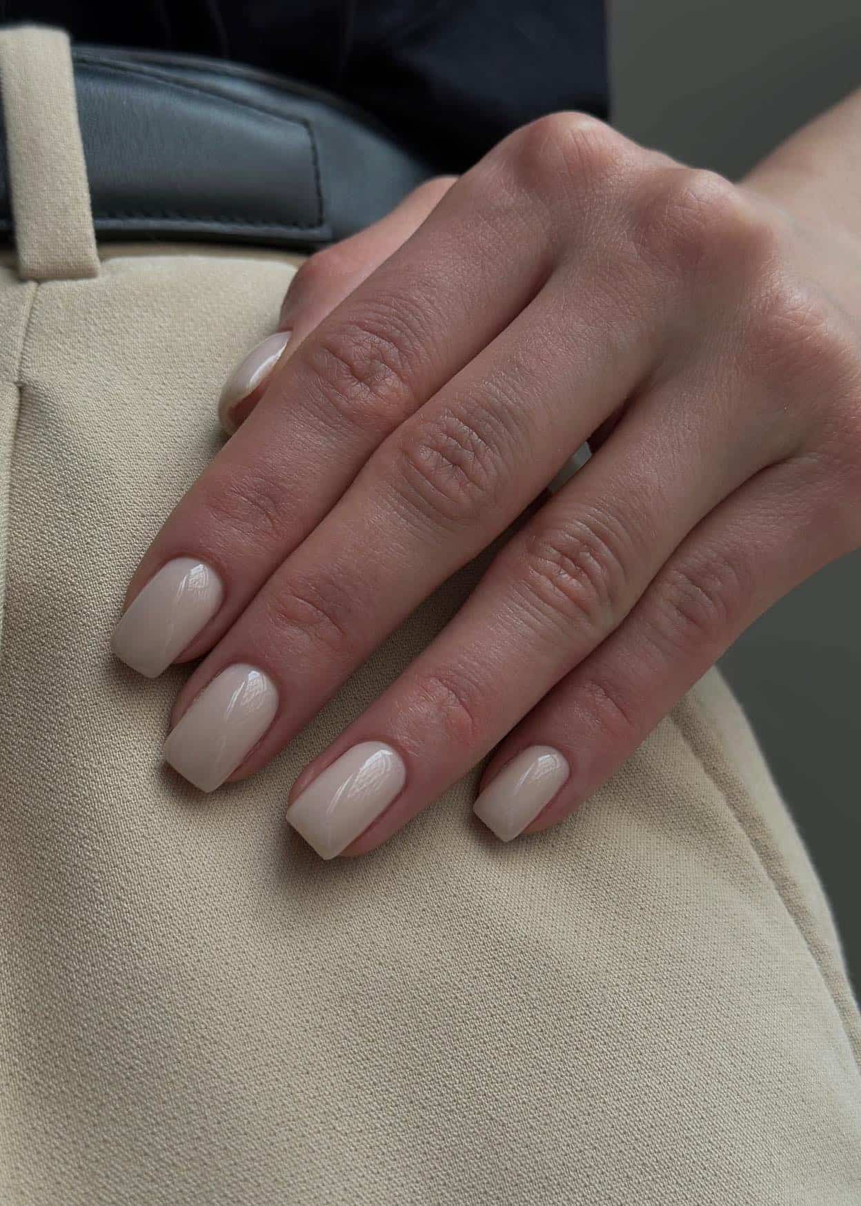 A hand with short square nails painted a glossy soft beige