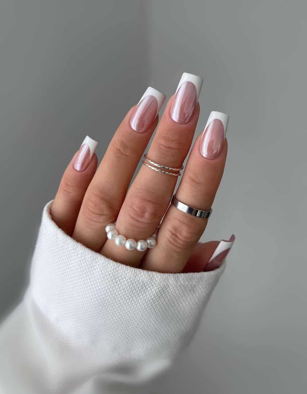 A hand with medium-length square nails painted with classic white French tips and a chrome finish