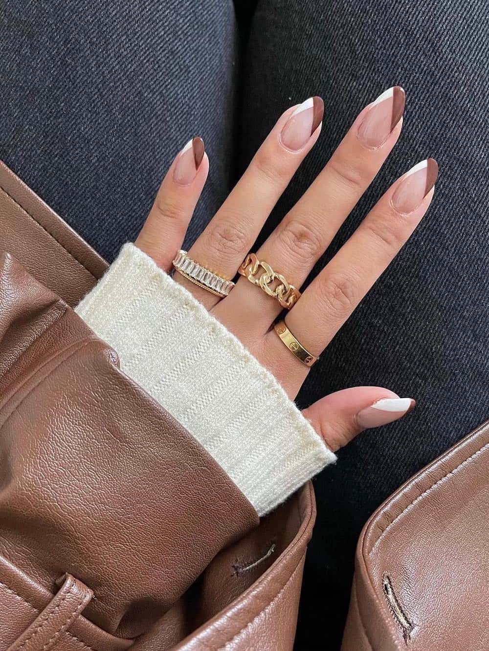 A hand with medium-length almond nails painted a glossy nude with white and brown slanted French tips