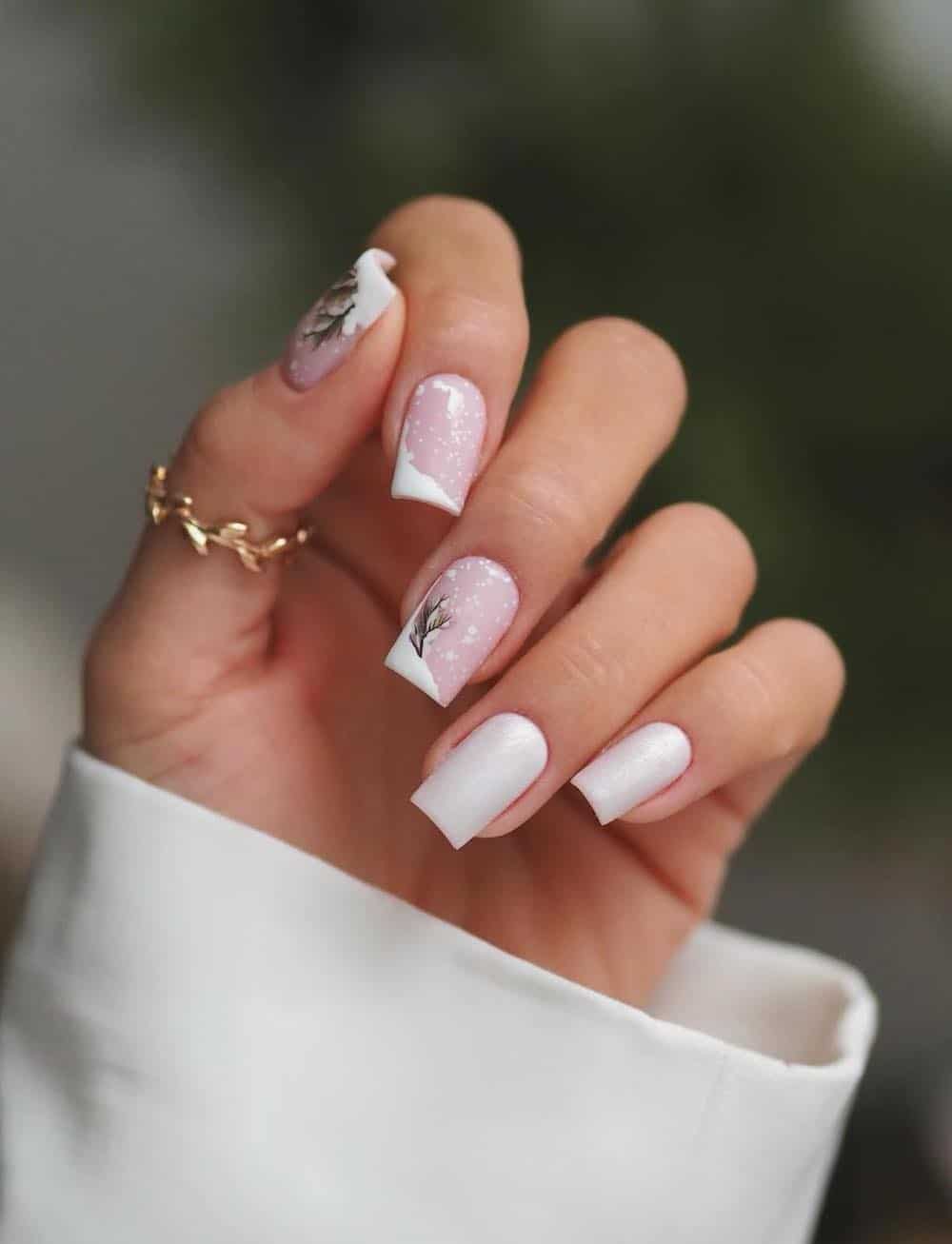 A hand with medium square nails painted a soft pink with white snow nail art and two glossy white accent nails
