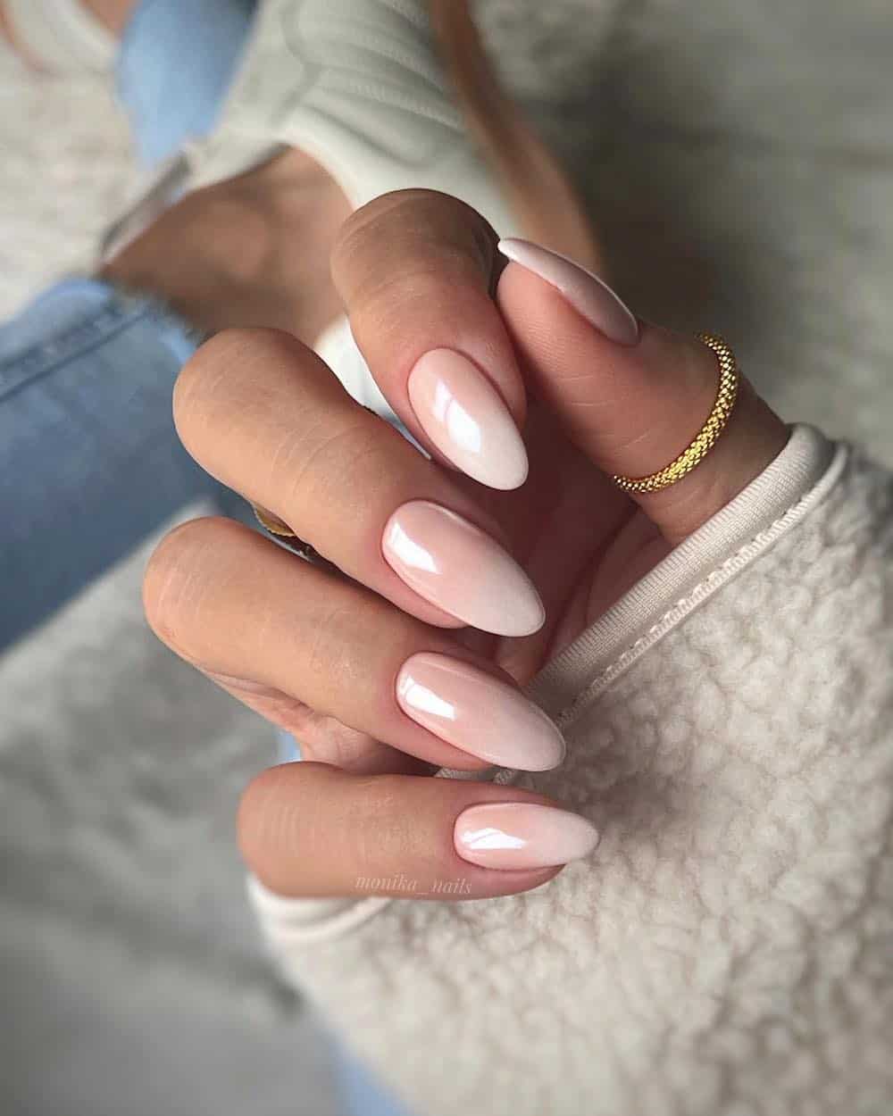 A hand with long almond nails painted a nude pink to cream ombre with a metallic finish