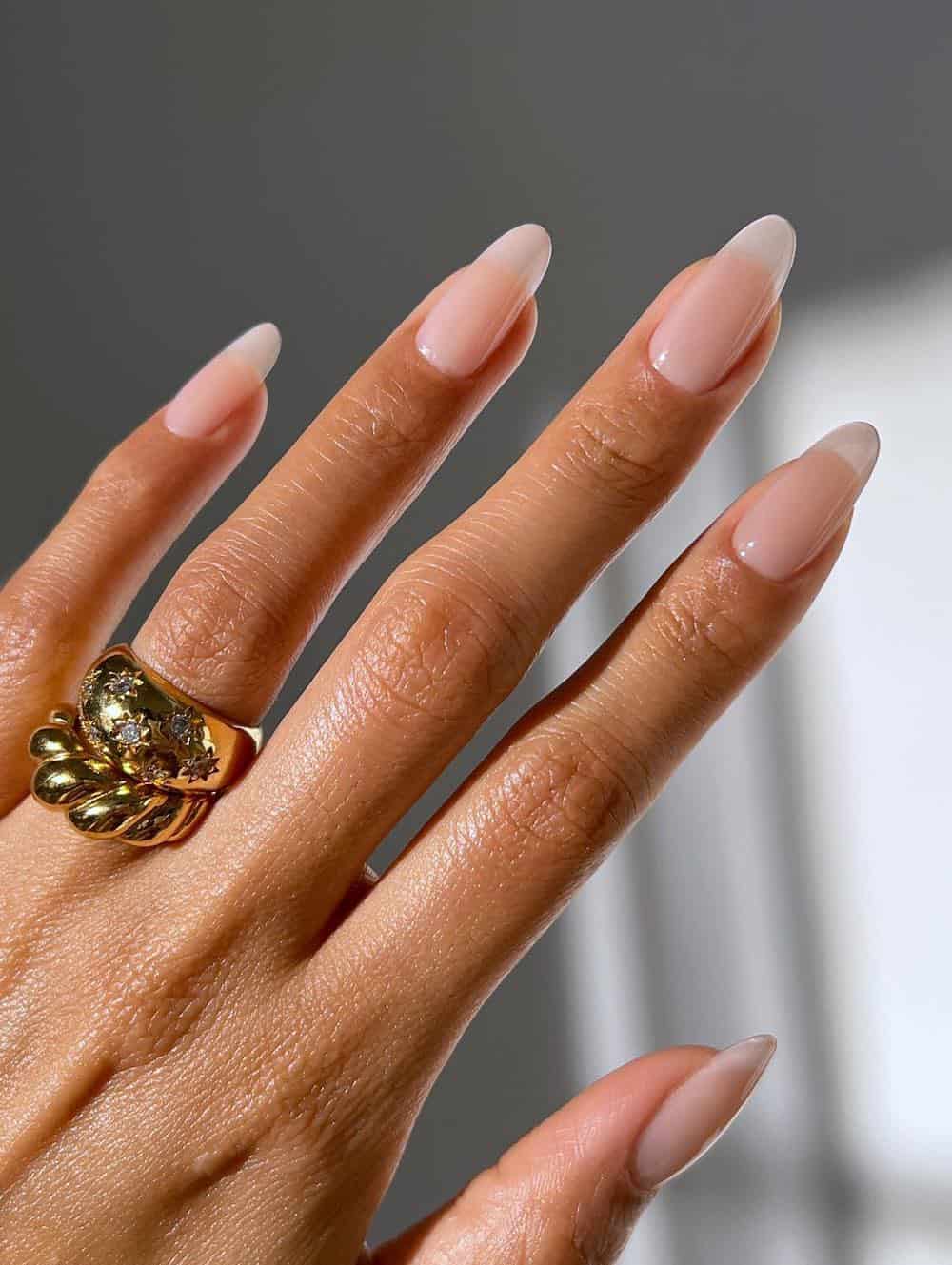 A hand with medium-length almond nails painted a glossy nude