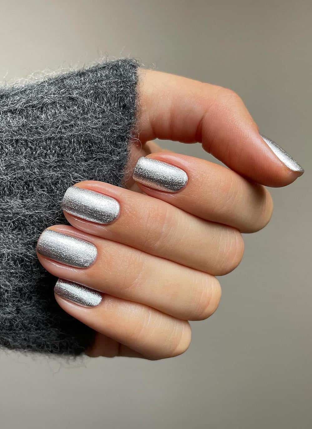 A hand with short square nails painted a metallic silver shade