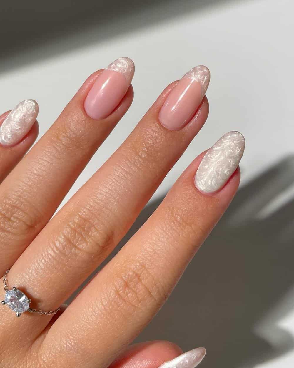 A hand with short almond nails painted a swirling pearly white with French tip accents