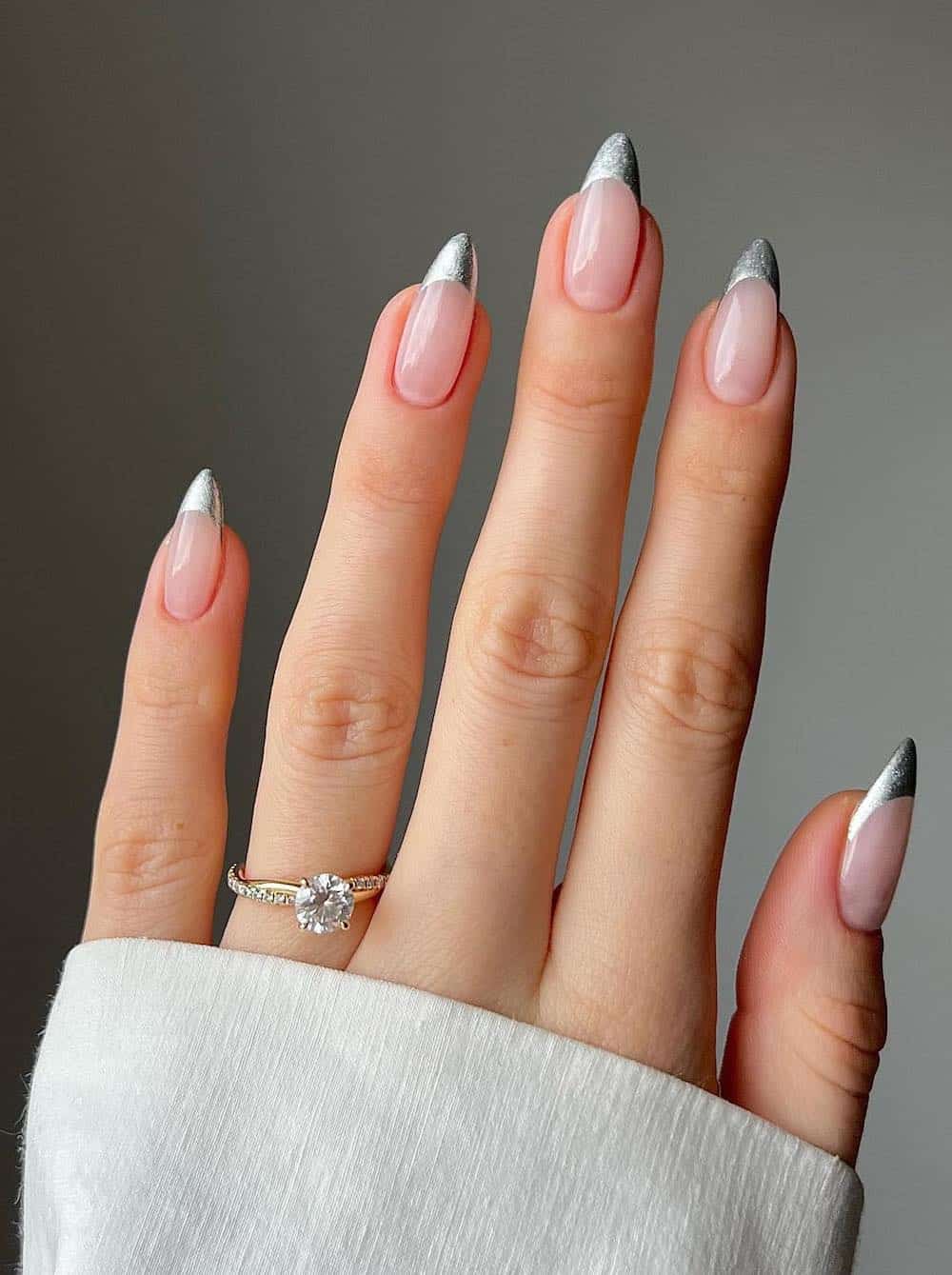 A hand with medium nude almond nails with metallic silver French tips