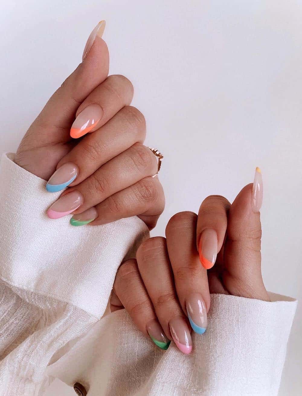 A hand with medium nude almond nails featuring colorful side French tips