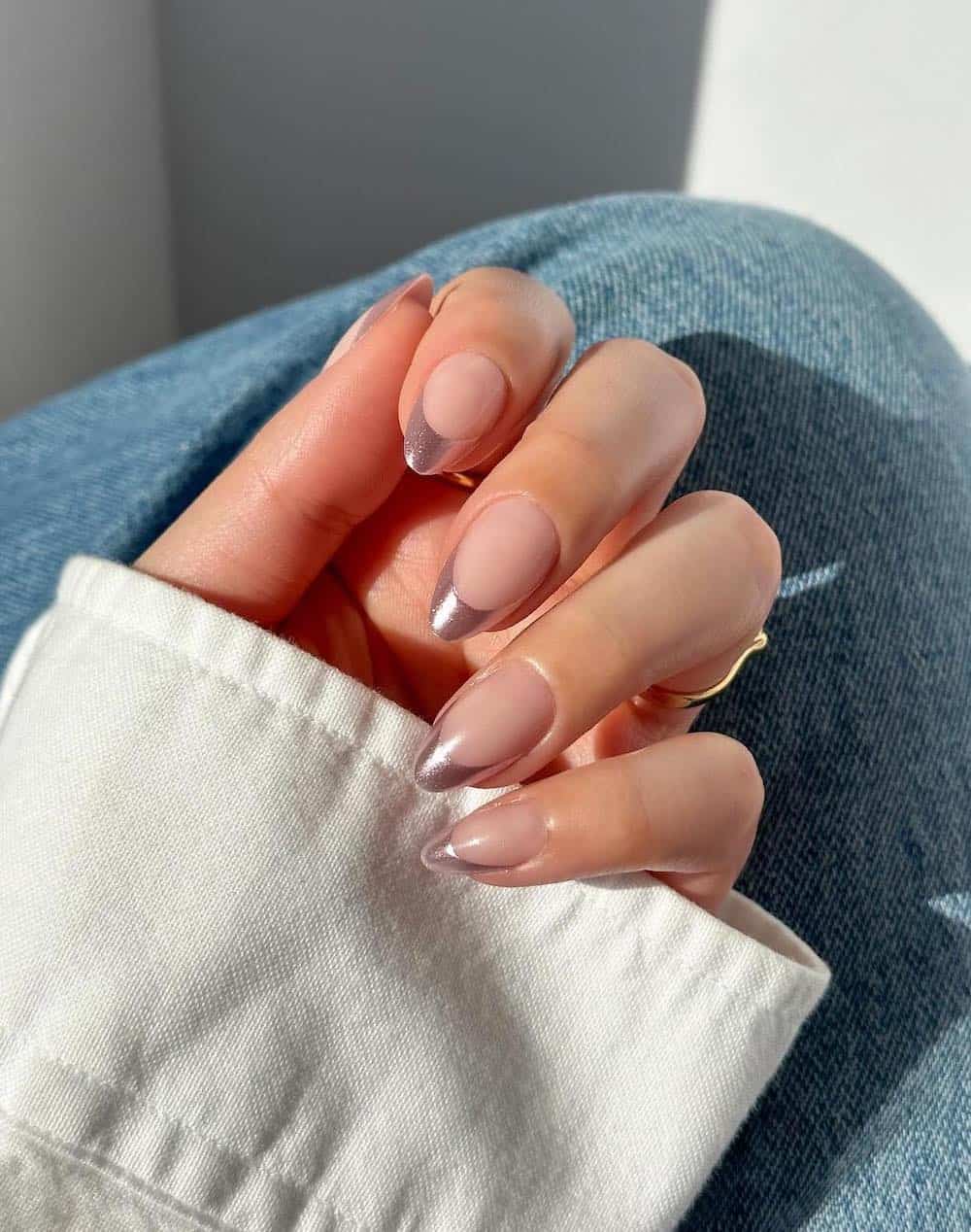 A hand with medium almond nails painted with metallic soft pink French tips