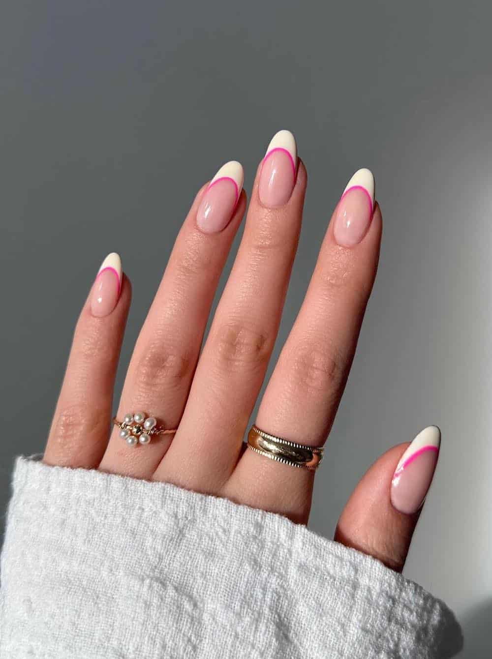 A hand with medium nude almond nails with pale yellow tips and bright pink thin lines underneath