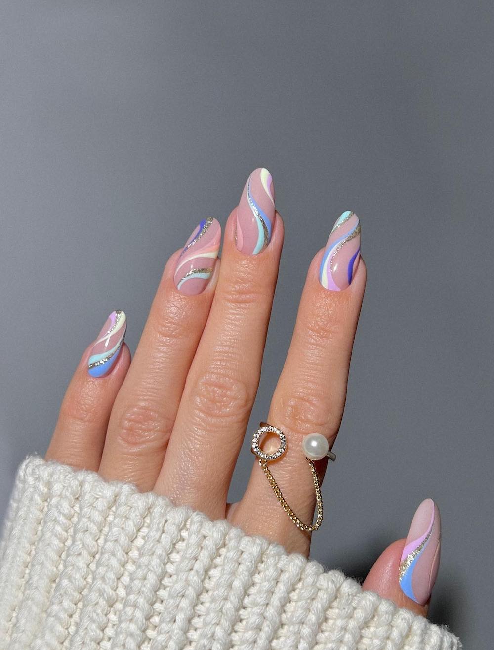 A hand with long nude almond nails with light blue, green, pink, purple, white, and silver glitter waves