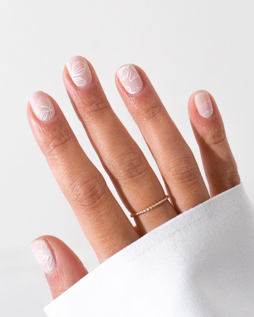 A hand with short milky white nails with white floral outlines