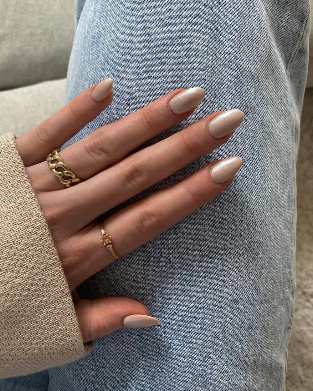 A hand with short almond nails painted a beige chrome