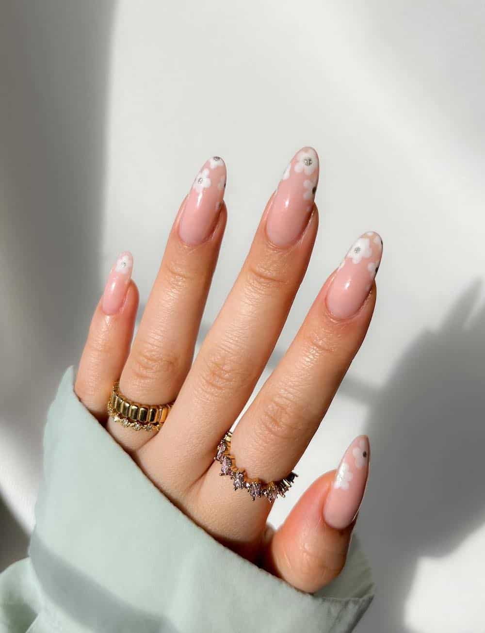 A hand with long nude almond nails with white flower French tips and silver centers