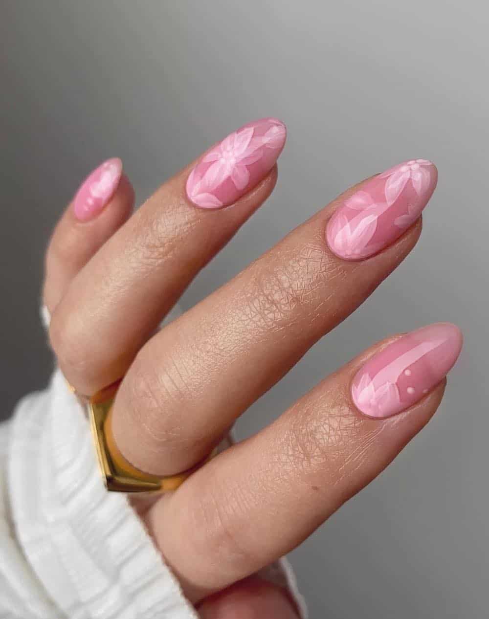 A hand with medium almond nails painted a light pink jelly polish with pink floral nail art
