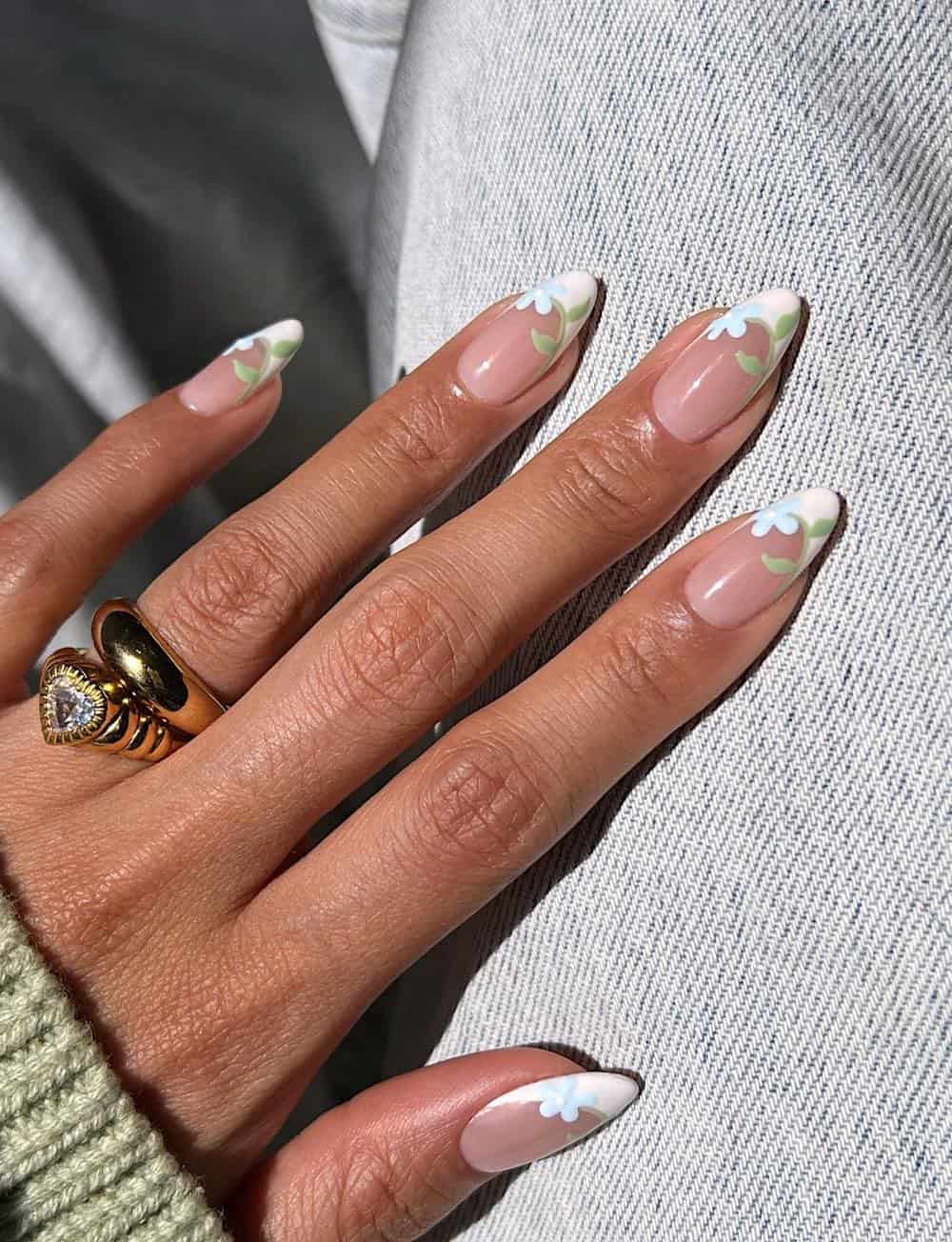 A hand with medium almond nails painted with white French tips with blue flowers and green leaves