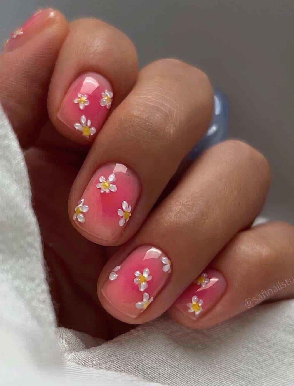 A hand with short pink jelly nails with dainty white flowers