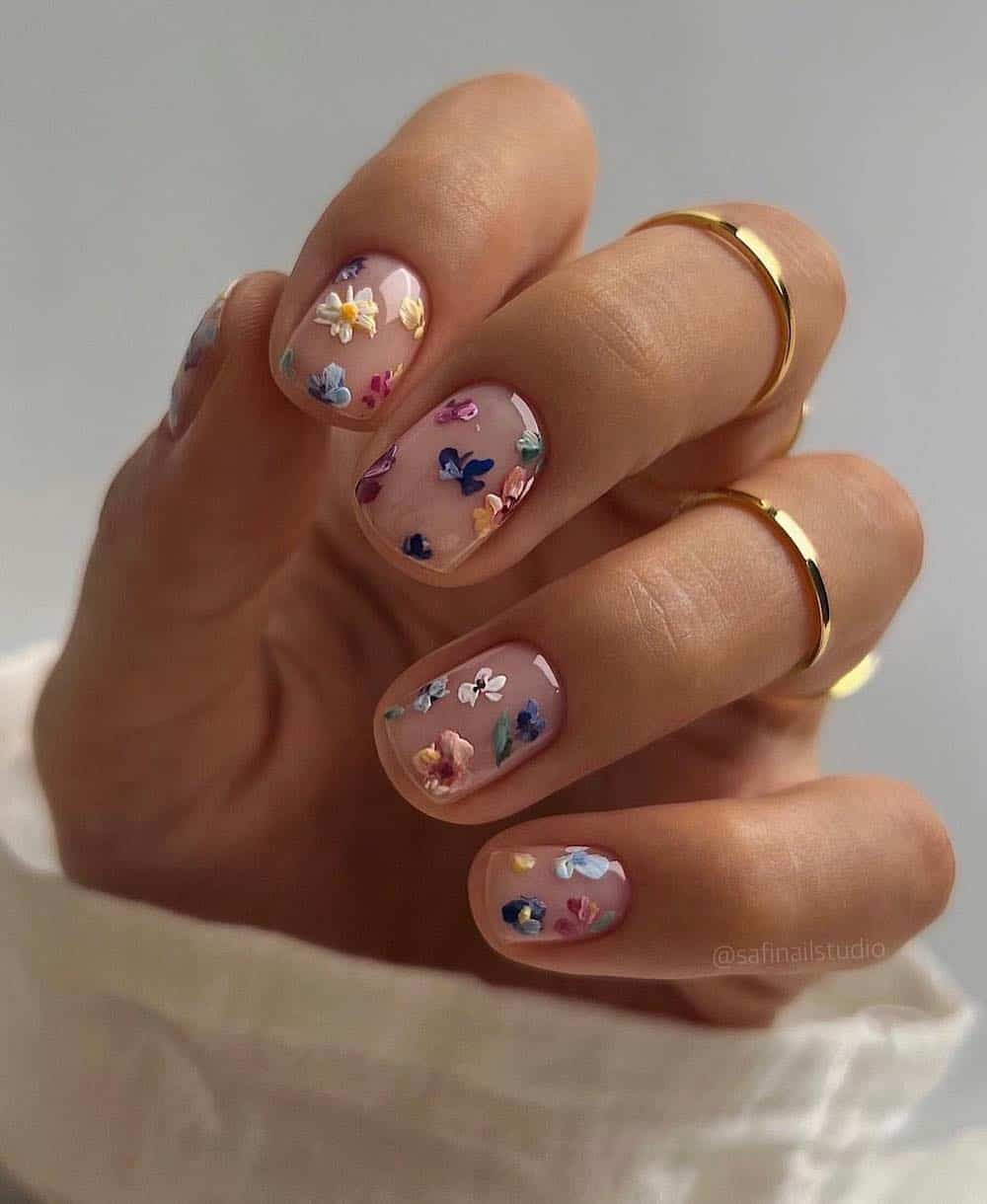 A hand with short nude nails painted with a multi-color floral design