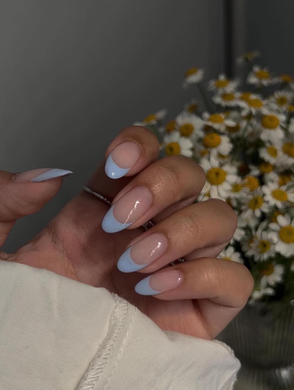 A hand with medium long nude nails painted with light blue French tips