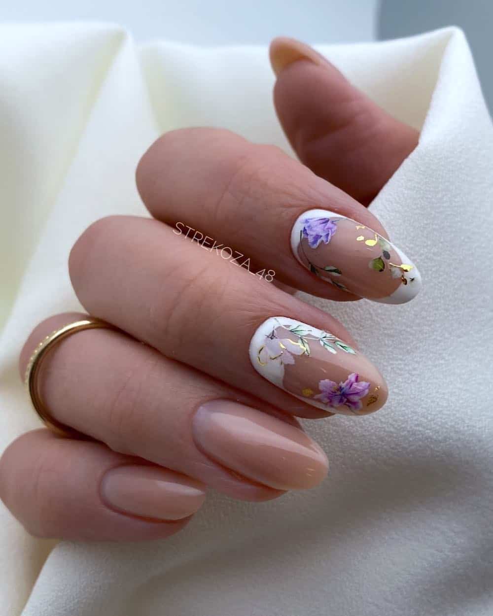 A hand with medium nude round nails with two accent nails featuring floral art and white accents