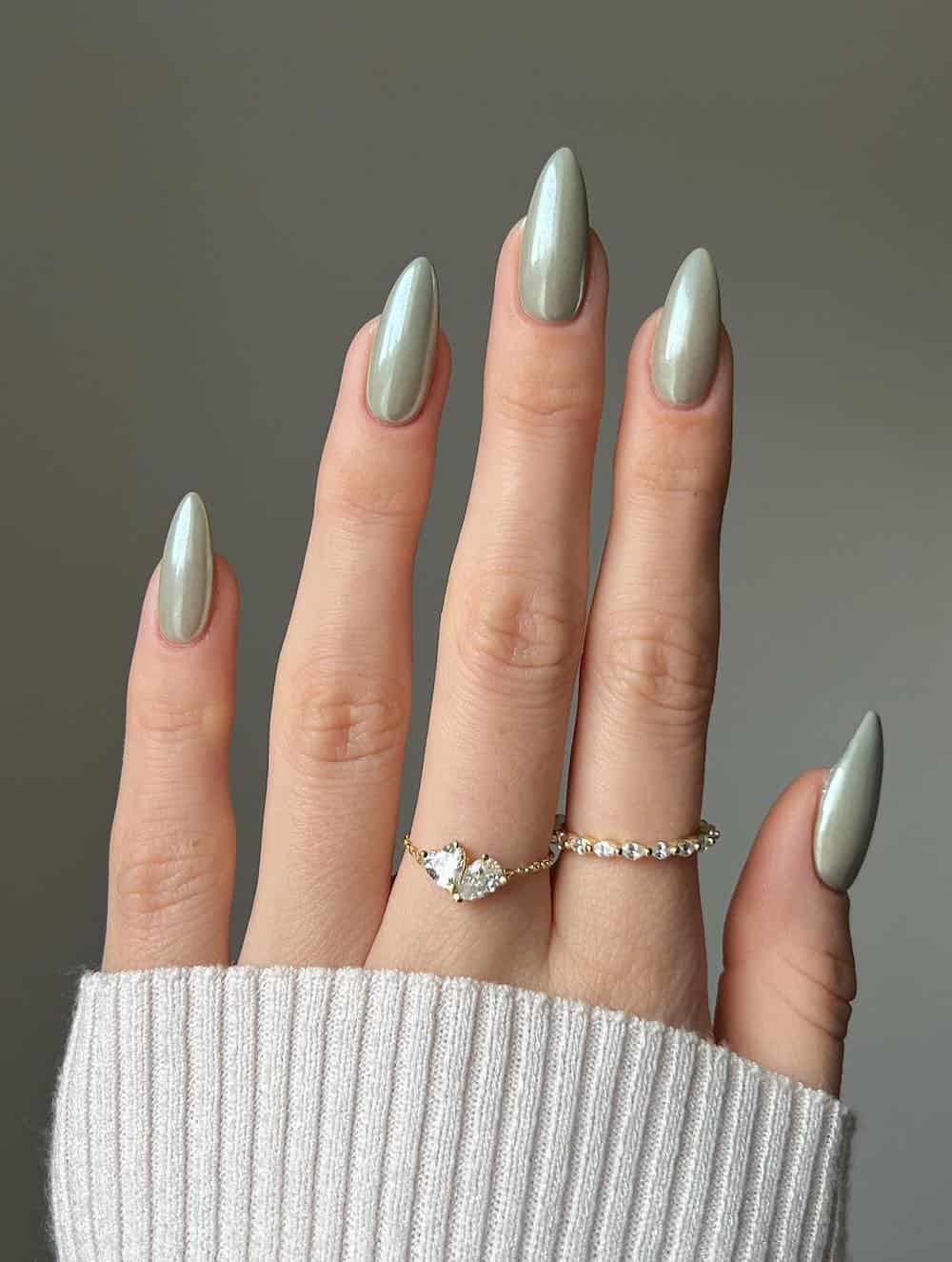 A hand with long almond nails painted a soft sage chrome