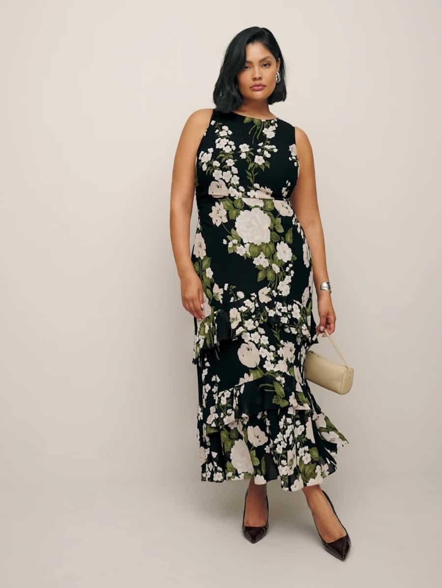 A woman wearing a black sleeveless maxi dress with a white floral print and green leaf pattern