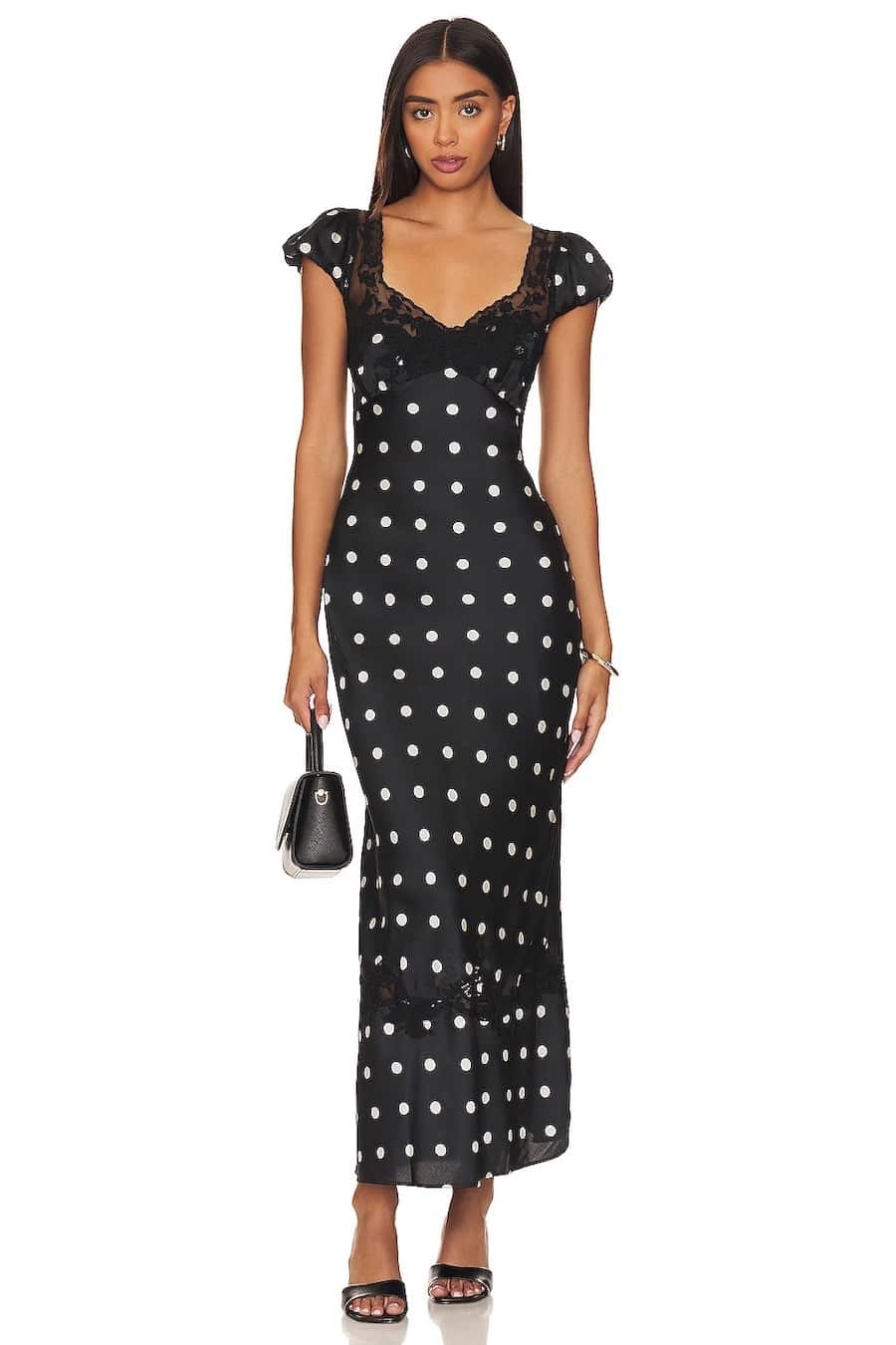 A woman wearing a black maxi dress with white polka dots with cap sleeves and a lace detail bodice
